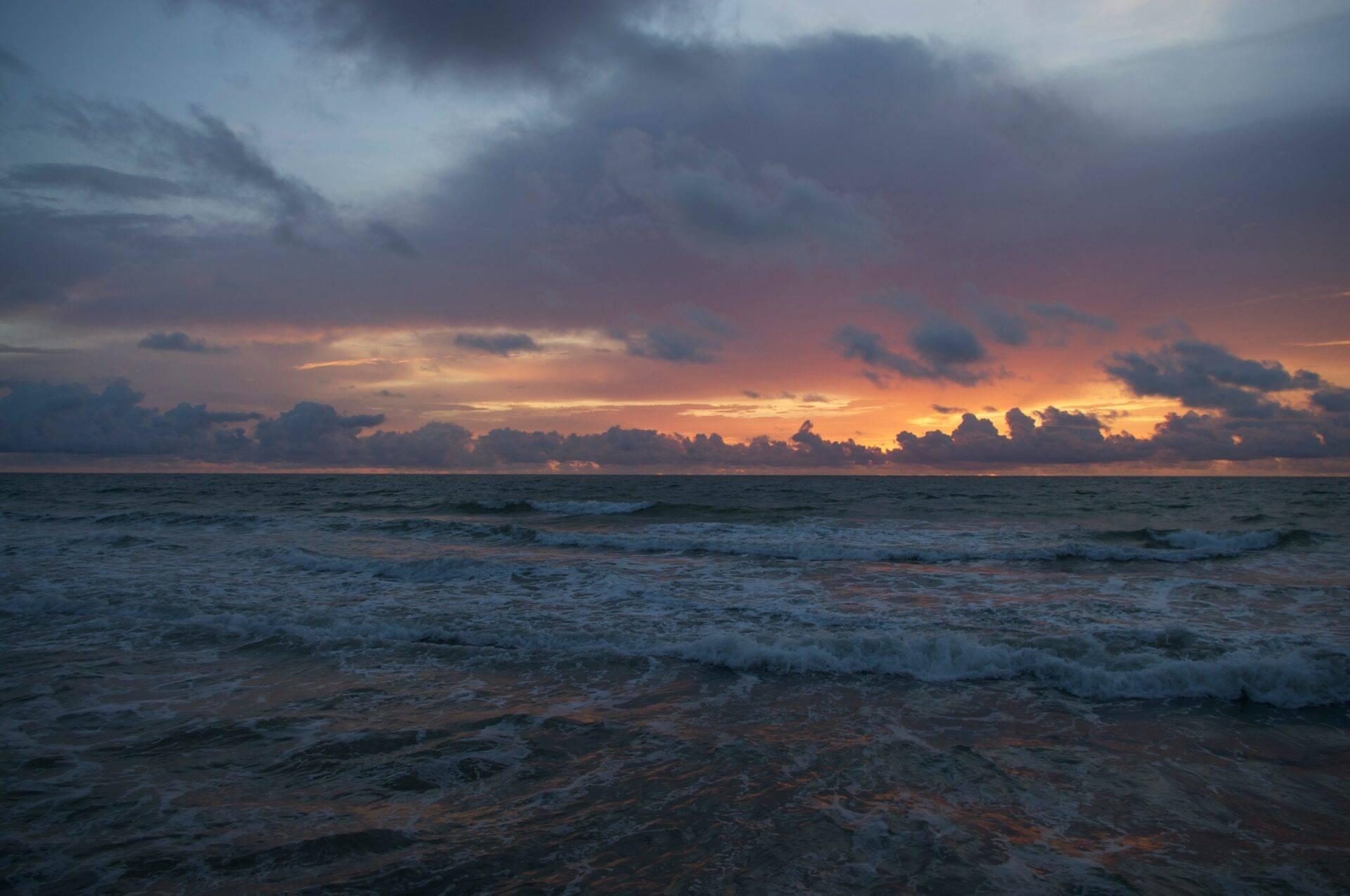 Spektakulärer Meeressonnenuntergang mit goldenen Wolken und Wellen auf einem menschenleeren Strand