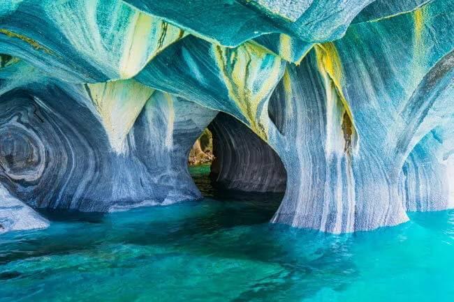 Grottes calcaires sculptées aux parois bleu-blanc surplombant une eau turquoise cristalline