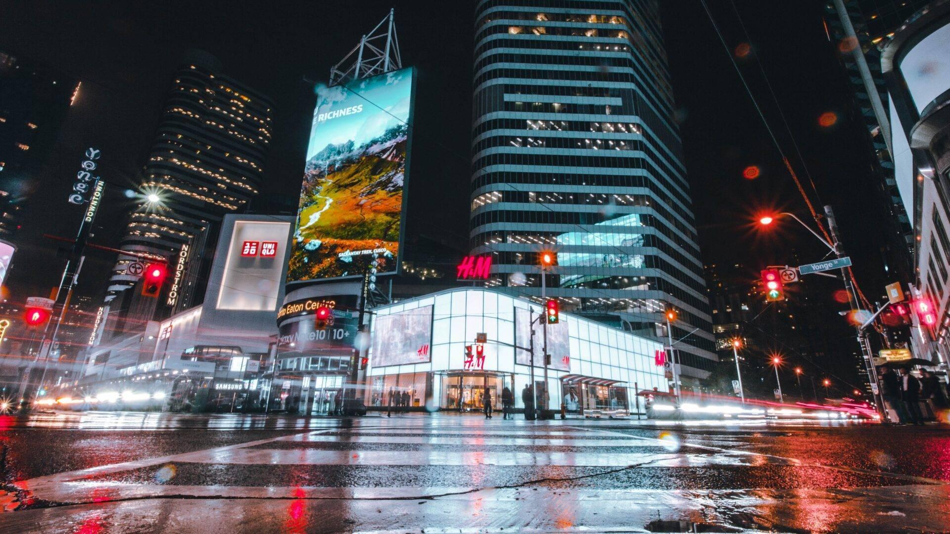 Eine lebhafte Einkaufsstraße bei Nacht mit beleuchteten Gebäuden, strahlenden Schaufenstern und Reflexionen auf dem nassen Asphalt