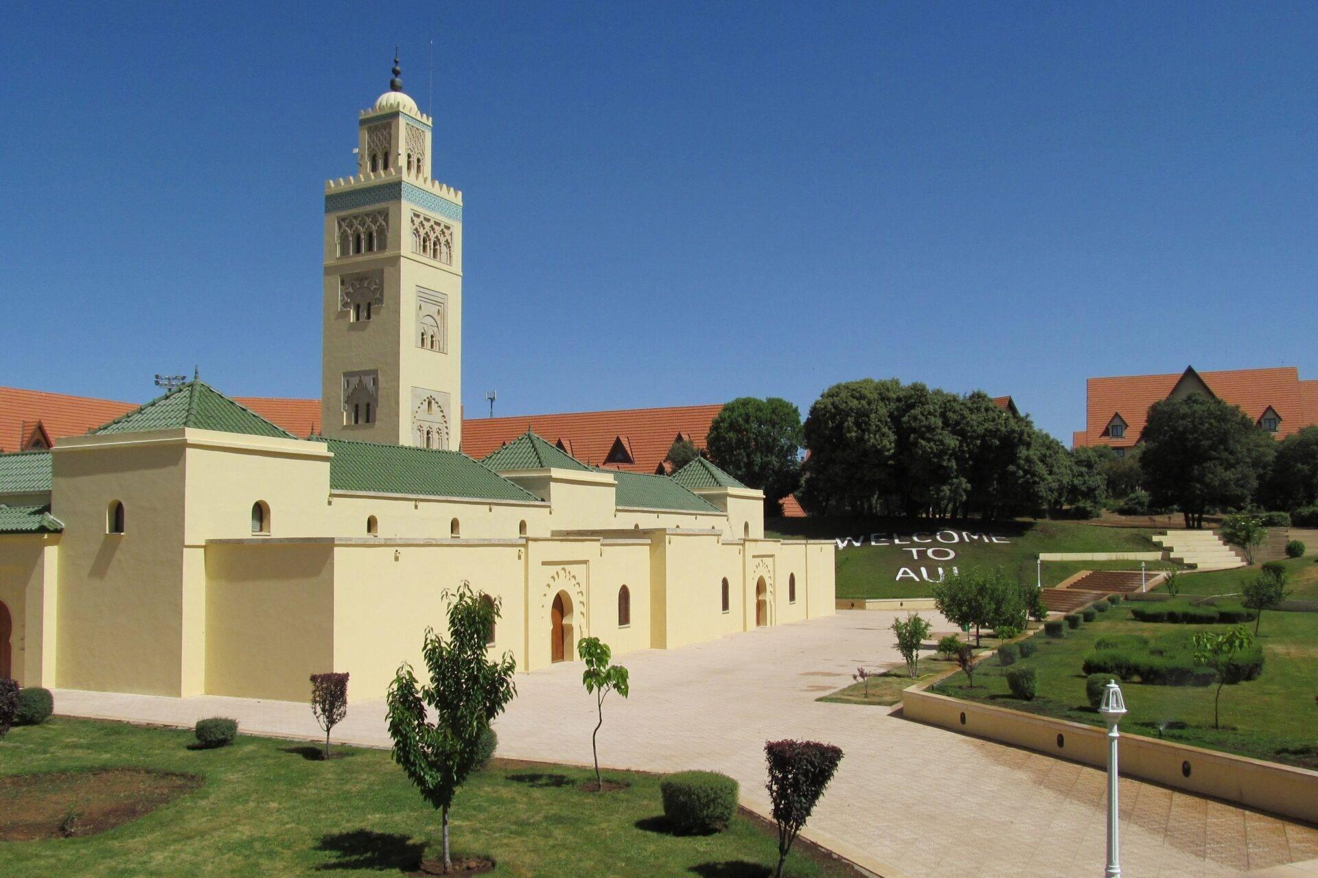 Moderne marokkanische Moschee mit schlankem Minarett, gepflastertem Innenhof und orangefarbenen Dächern unter blauem Himmel