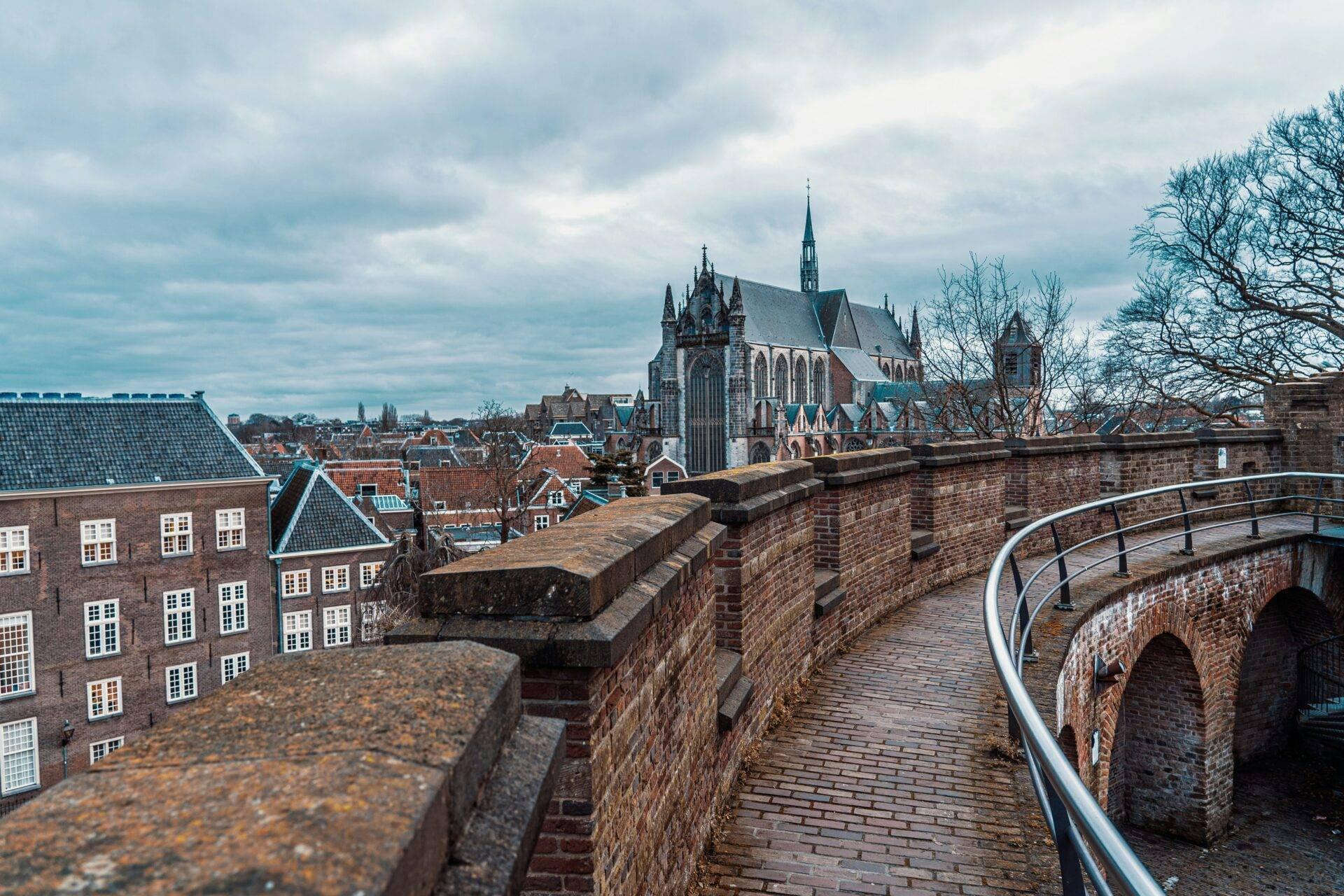 Blick von einer Stadtmauer auf eine gotische Kirche, Backsteinhäuser und bewölkten Himmel in einer niederländischen Stadt