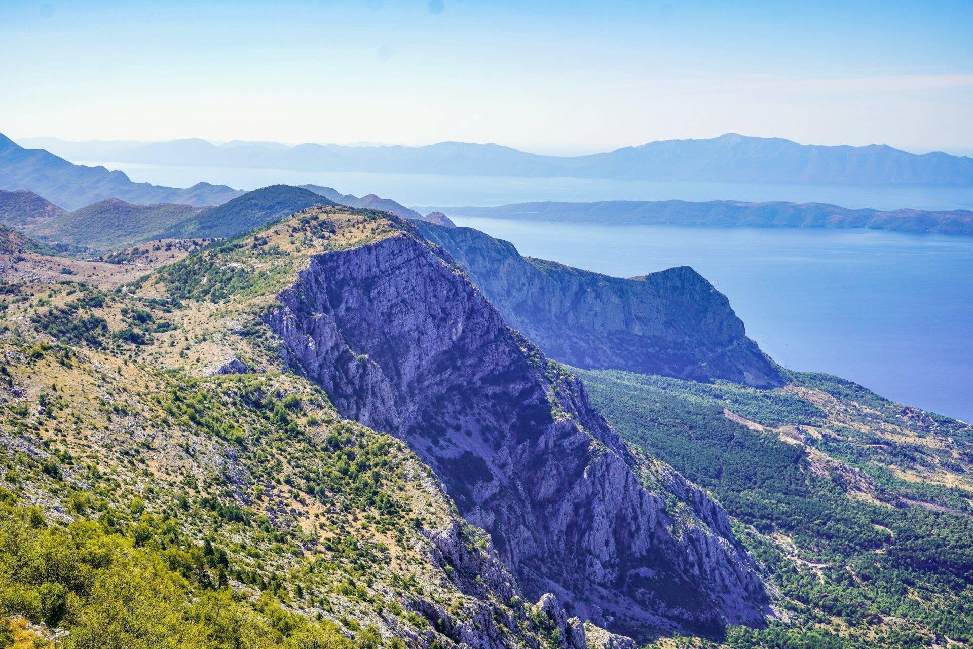 Vista panoramica su montagne calcaree scoscese che dominano un mare Mediterraneo turchese e isole lontane