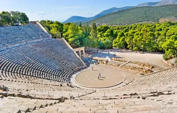Ein antikes Steintheater mit halbkreisförmigen Sitzreihen, eingebettet in mediterrane Grünflächen und Berge