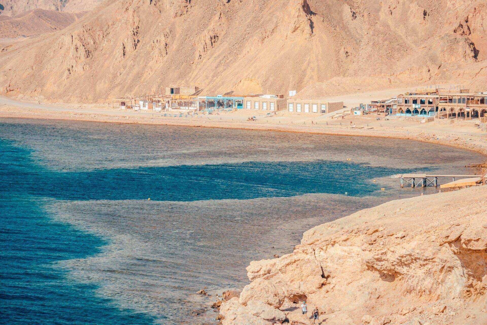 Una spiaggia deserta in Egitto con edifici costieri, montagne aride e un mare turchese cristallino