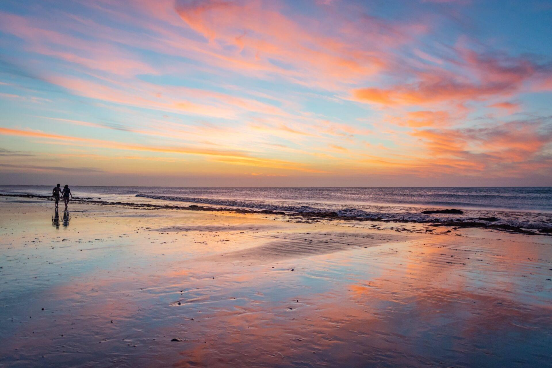 Zwei Surfer an einem Strand bei Sonnenuntergang mit goldenen Reflexionen auf dem nassen Sand