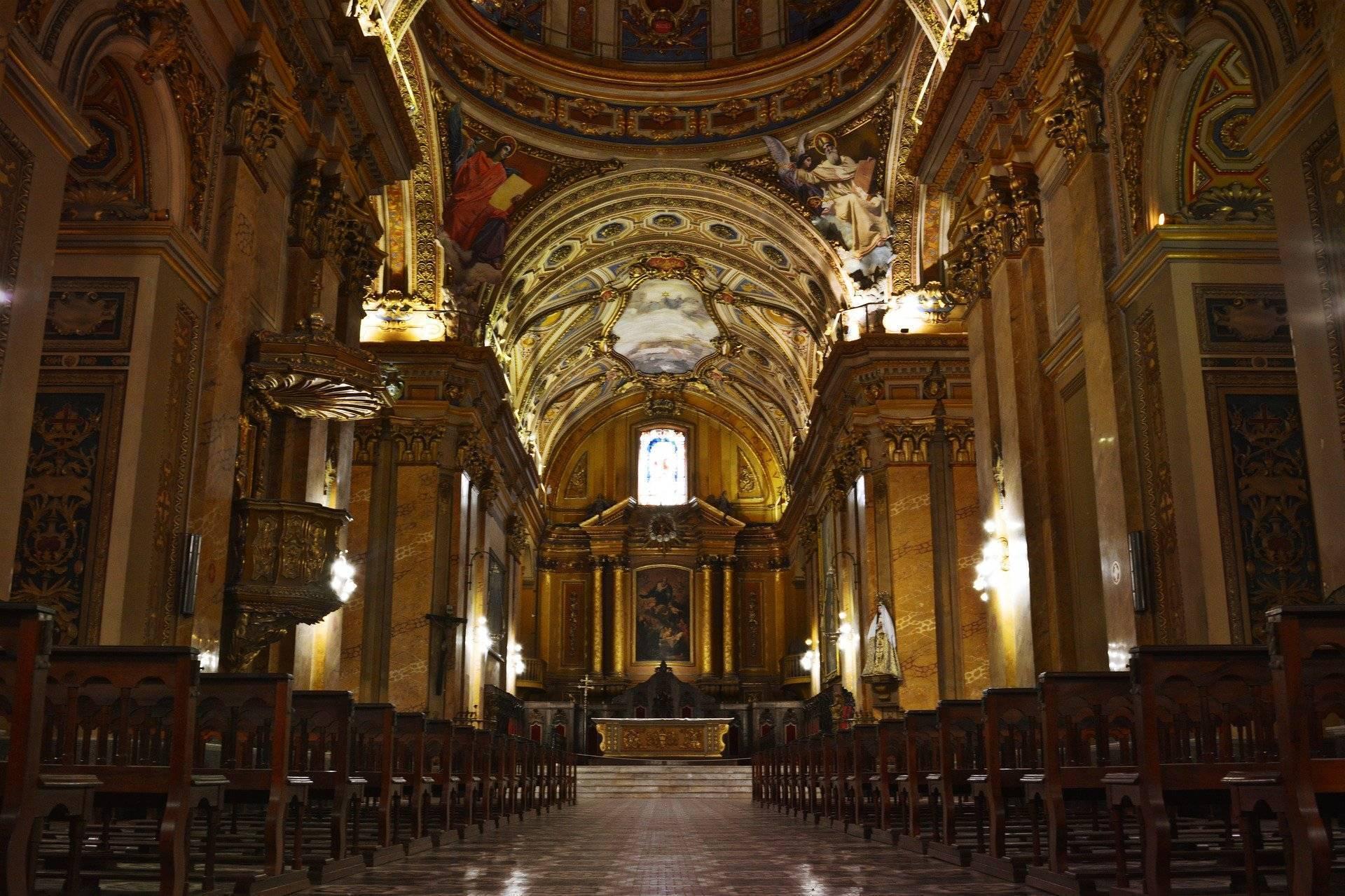 Interno maestoso di una basilica con navata centrale dorata, volta ornamentata e altare illuminato