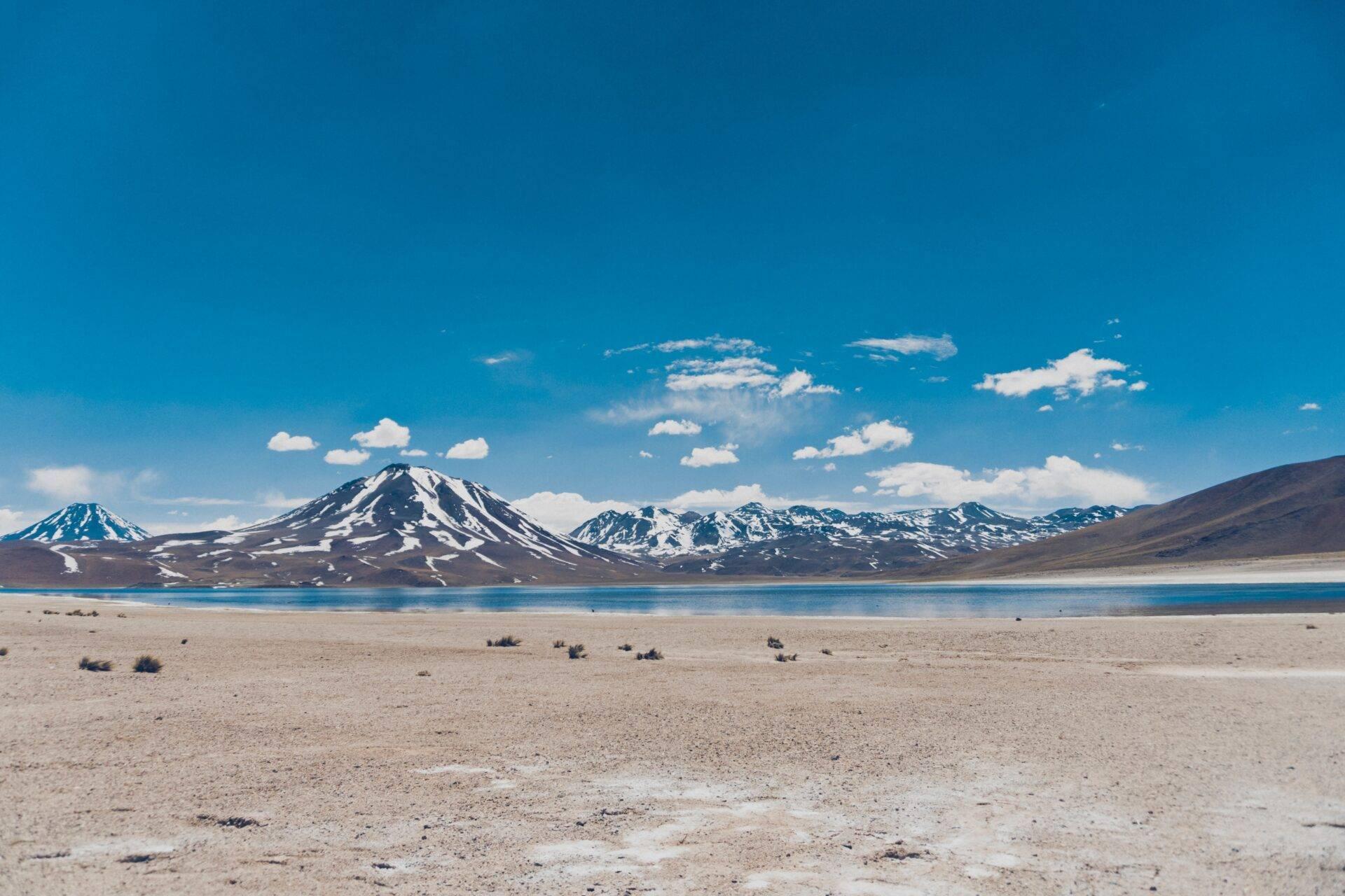 Deserto d’alta quota con lago turchese e vulcani innevati sotto un cielo terso