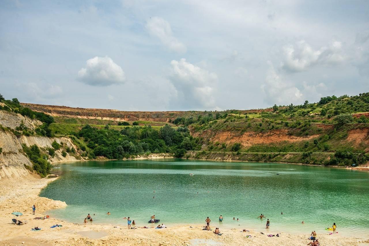 Ein türkisfarbener See umgeben von grünen Felsen mit Badegästen an einem weißen Sandstrand