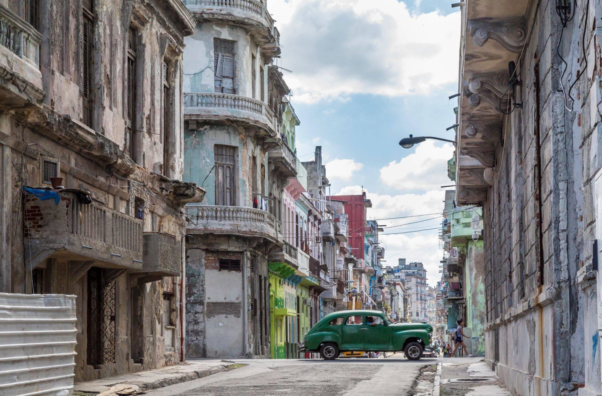 Una stradina storica stretta con facciate coloniali colorate e una vecchia auto verde parcheggiata