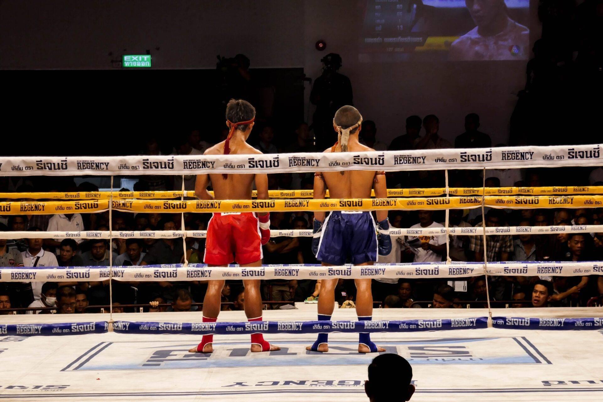 Due pugili sul ring durante un incontro di boxe thailandese in un’arena piena di spettatori