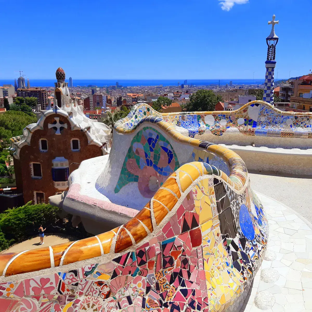 Panoramablick auf einen farbenfrohen Architekturpark mit Mosaiken, fantasievollen Häusern und blauem Meer im Hintergrund