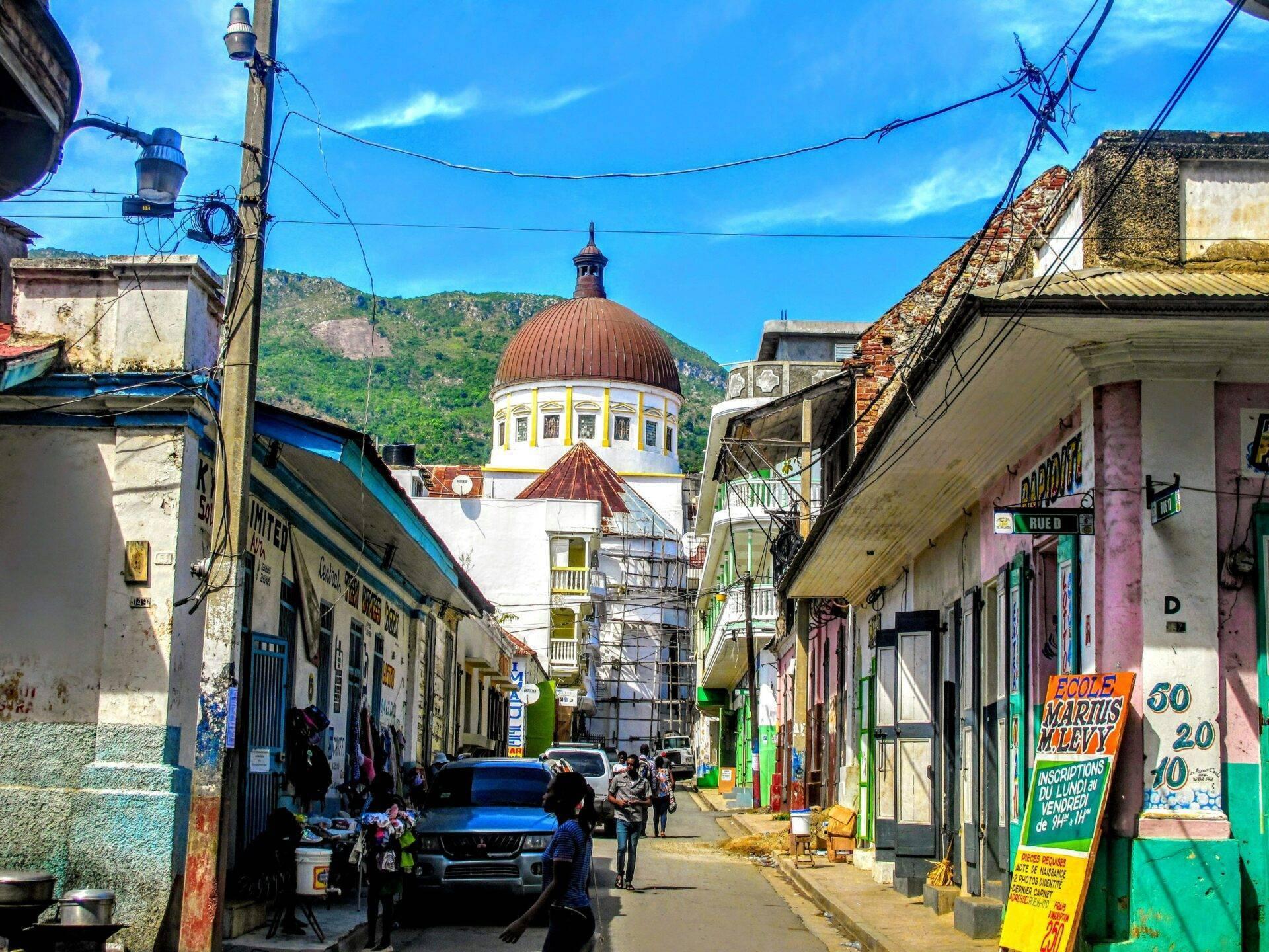 Una calle colorida de una ciudad caribeña con una iglesia de cúpula roja dominando el horizonte montañoso