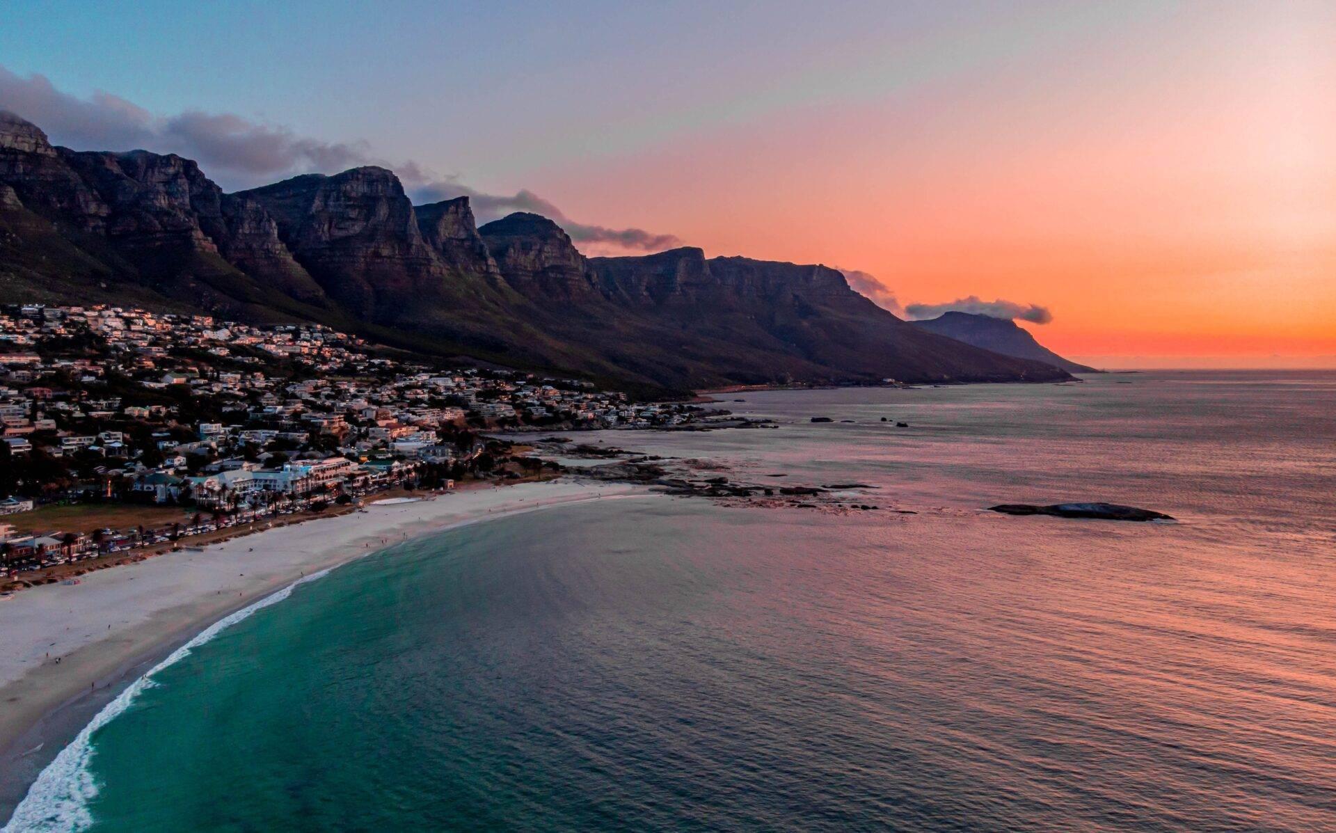 Sunset over a white sand beach facing majestic rocky mountains overlooking a coastal bay