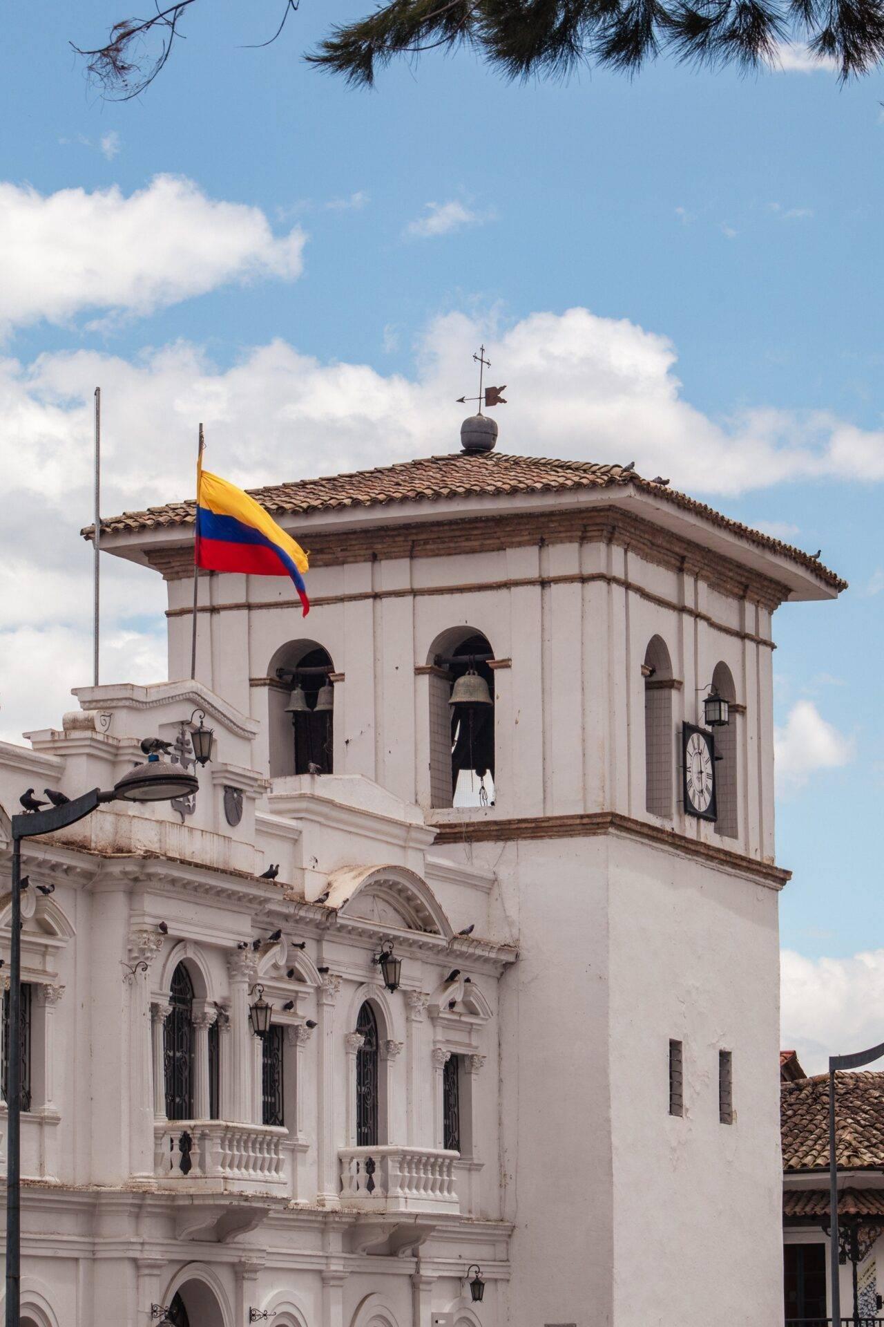 Iglesia colonial blanca con campanario y bandera colombiana ondeando bajo un cielo nublado