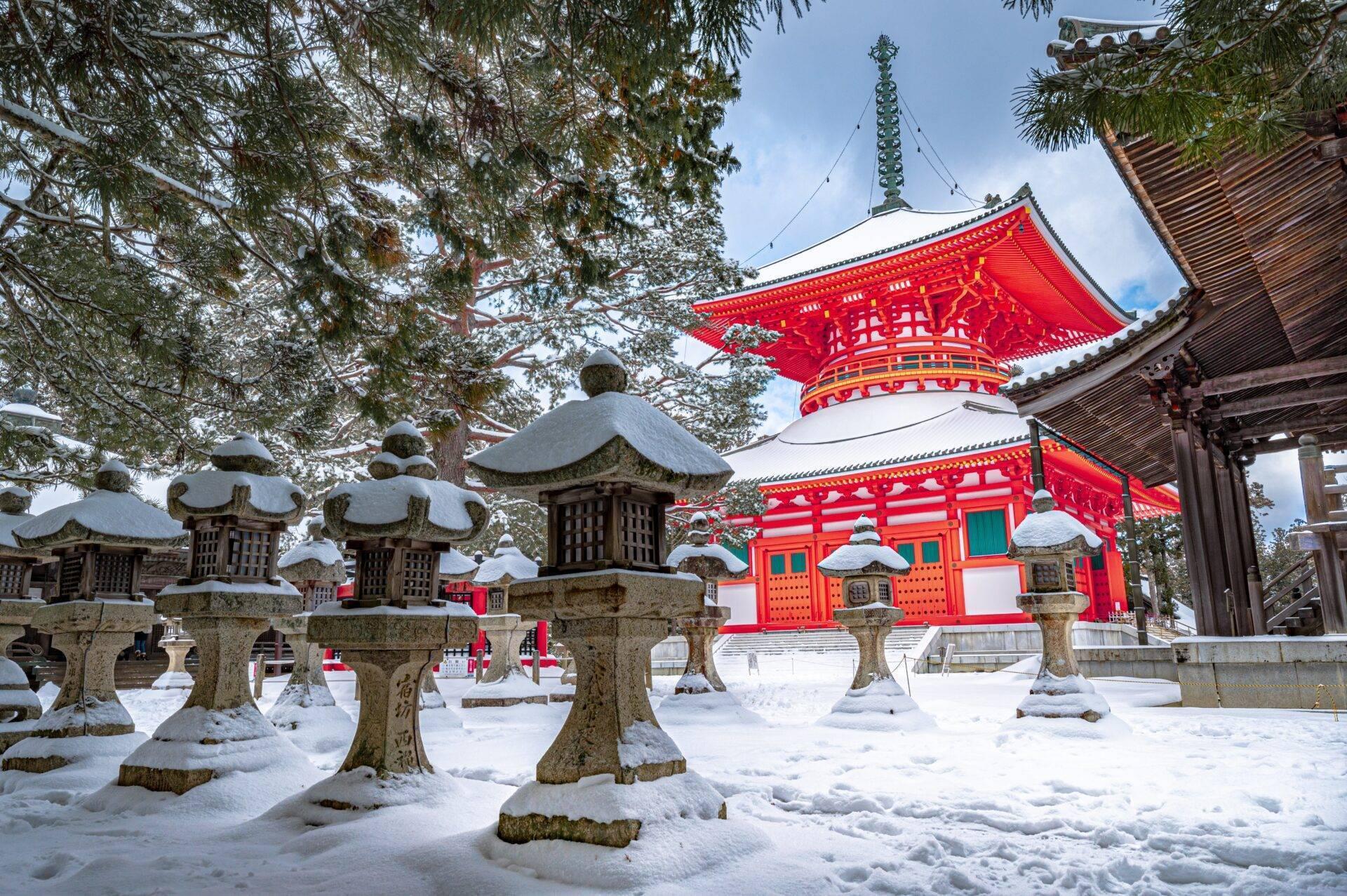Ein japanischer buddhistischer Tempel mit leuchtend roten Dächern, umgeben von schneebedeckten Steinlaternen unter bereiften Bäumen