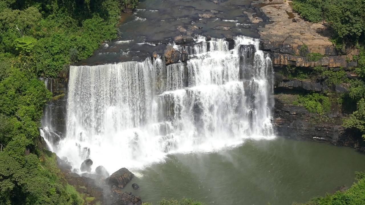 Una maestosa cascata a più livelli riversa le sue acque bianche spumeggianti in una vasca smeraldo, incorniciata da lussureggiante vegetazione tropicale
