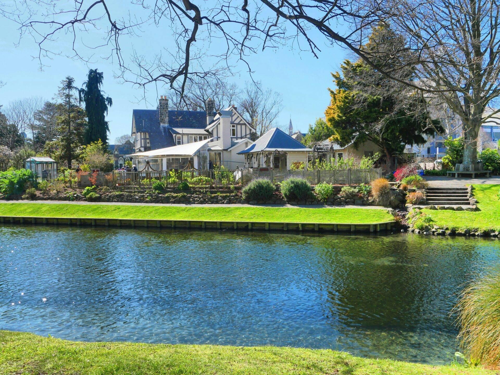 Una casa bianca sul bordo di un fiume con giardino fiorito e alberi spogli, paesaggio di campagna tranquilla e verdeggiante