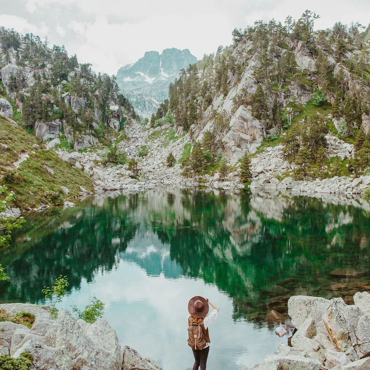 Eine Wanderin betrachtet einen kristallklaren Bergsee, eingerahmt von Felswänden und Tannenwäldern