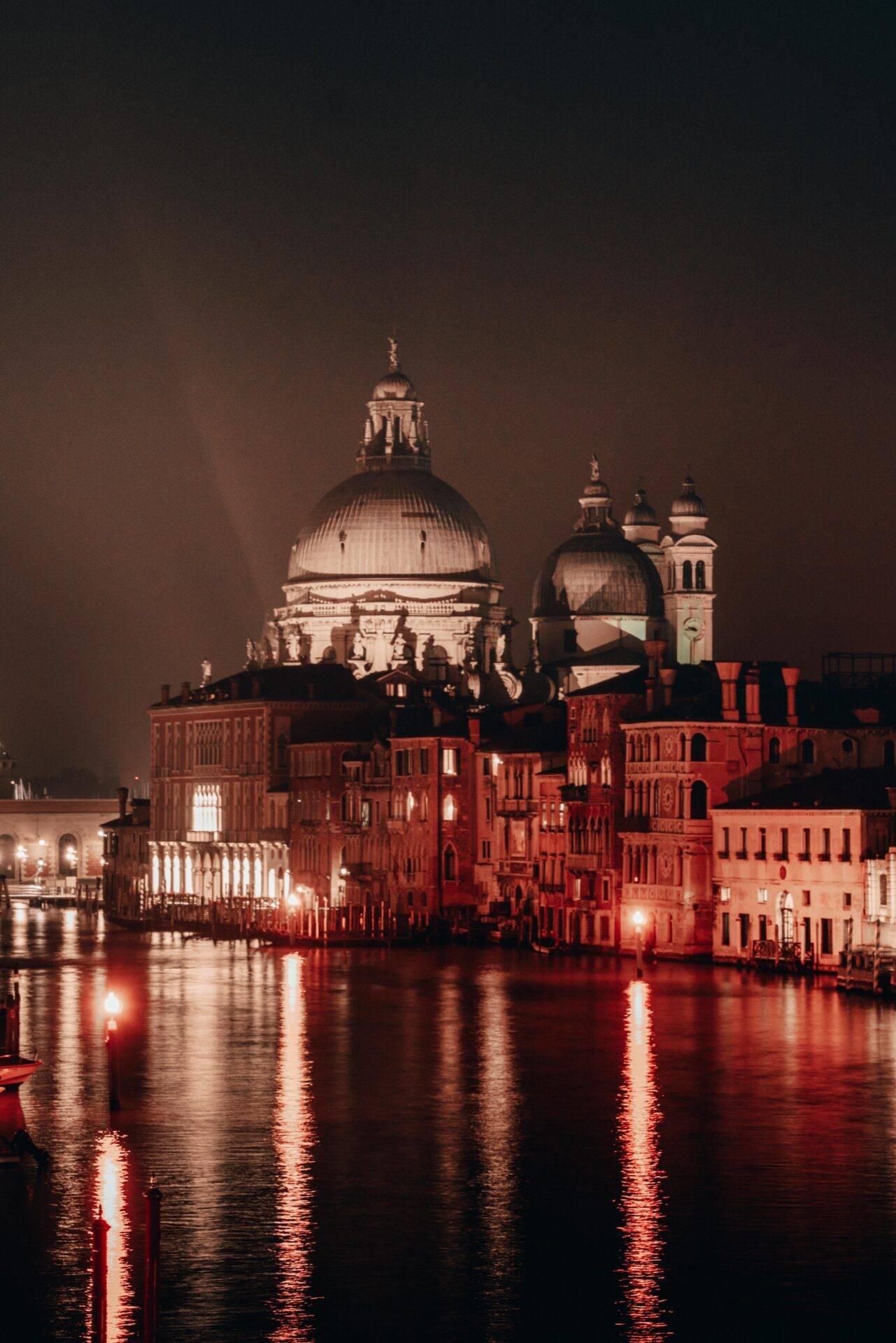 Vista notturna della Basilica della Salute illuminata sopra il Canal Grande con i suoi edifici storici in mattoni rossi