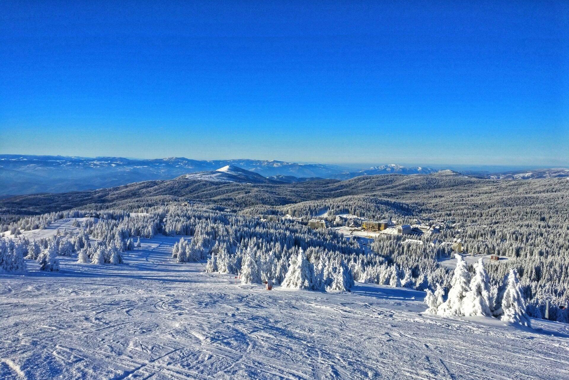 Luftaufnahme einer verschneiten Bergregion mit Nadelwäldern, zugefrorenen Seen und Gebäuden in einem Talkessel