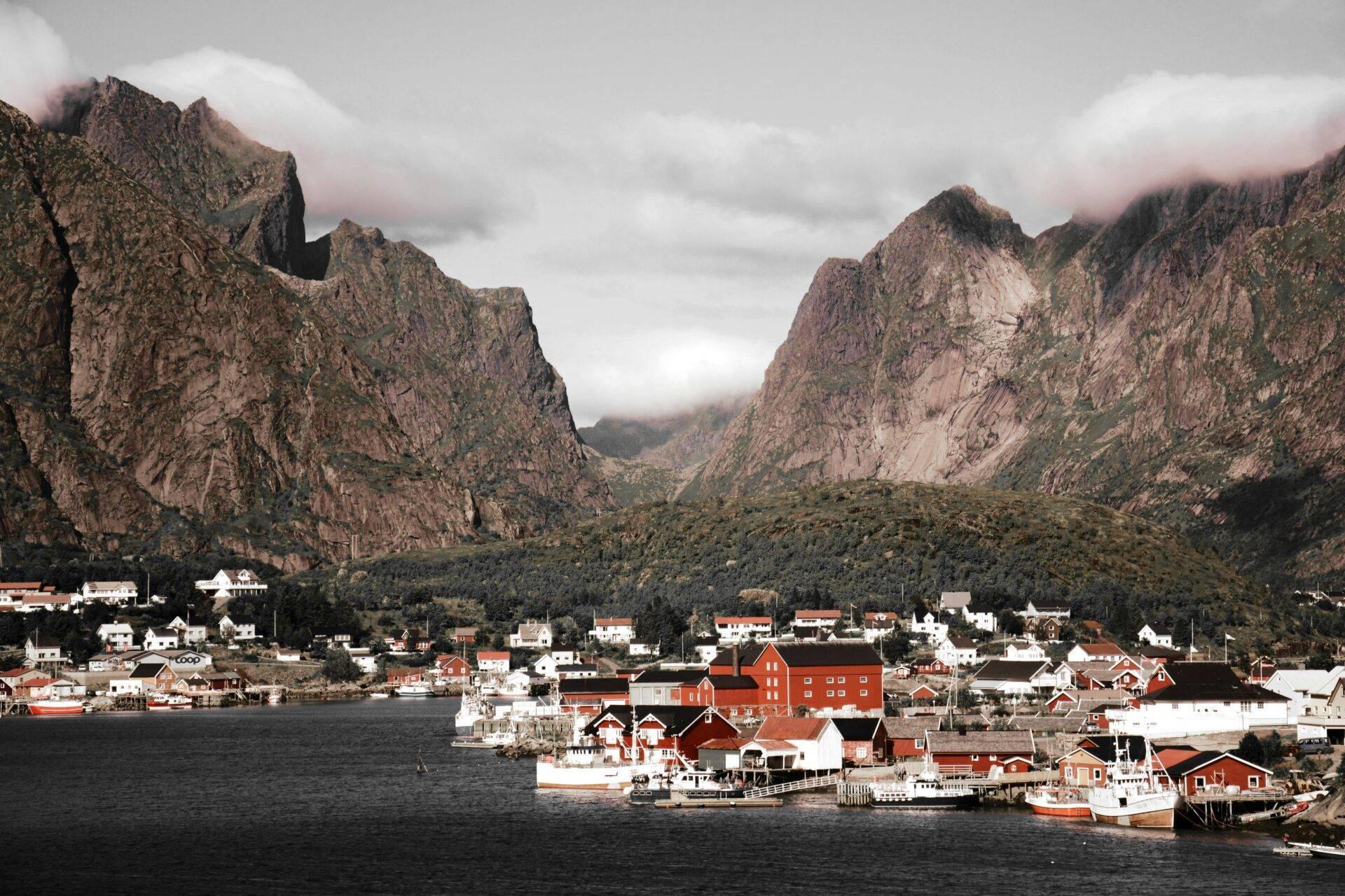 Kleines skandinavisches Küstendorf mit traditionellen roten Häusern, von steilen Bergen und Nebel umgeben