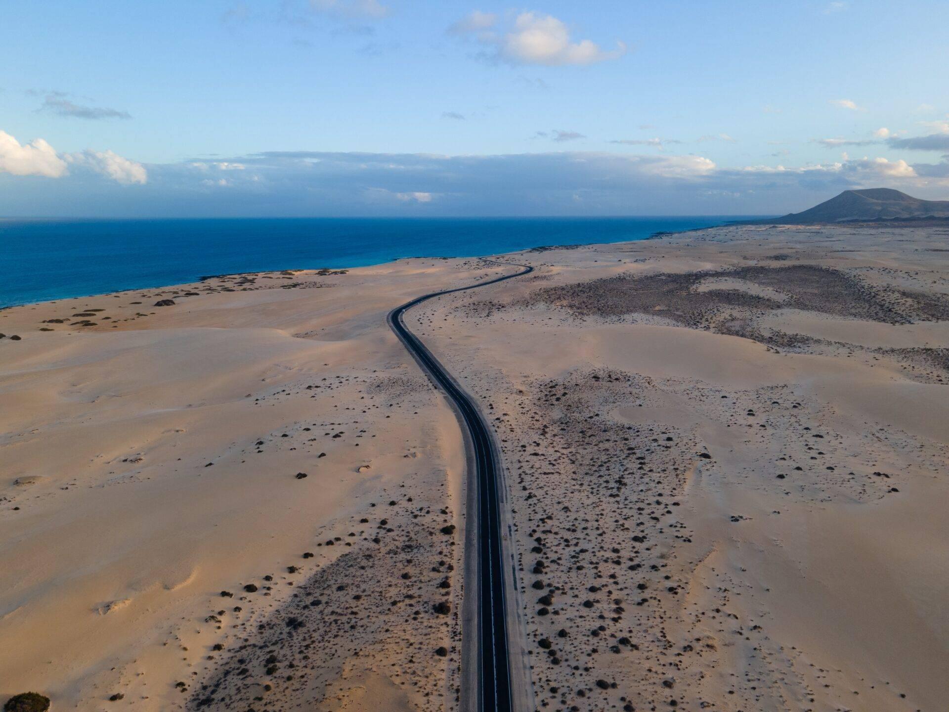 Strada asfaltata che attraversa un paesaggio vulcanico desertico verso il mare blu e un’isola sullo sfondo