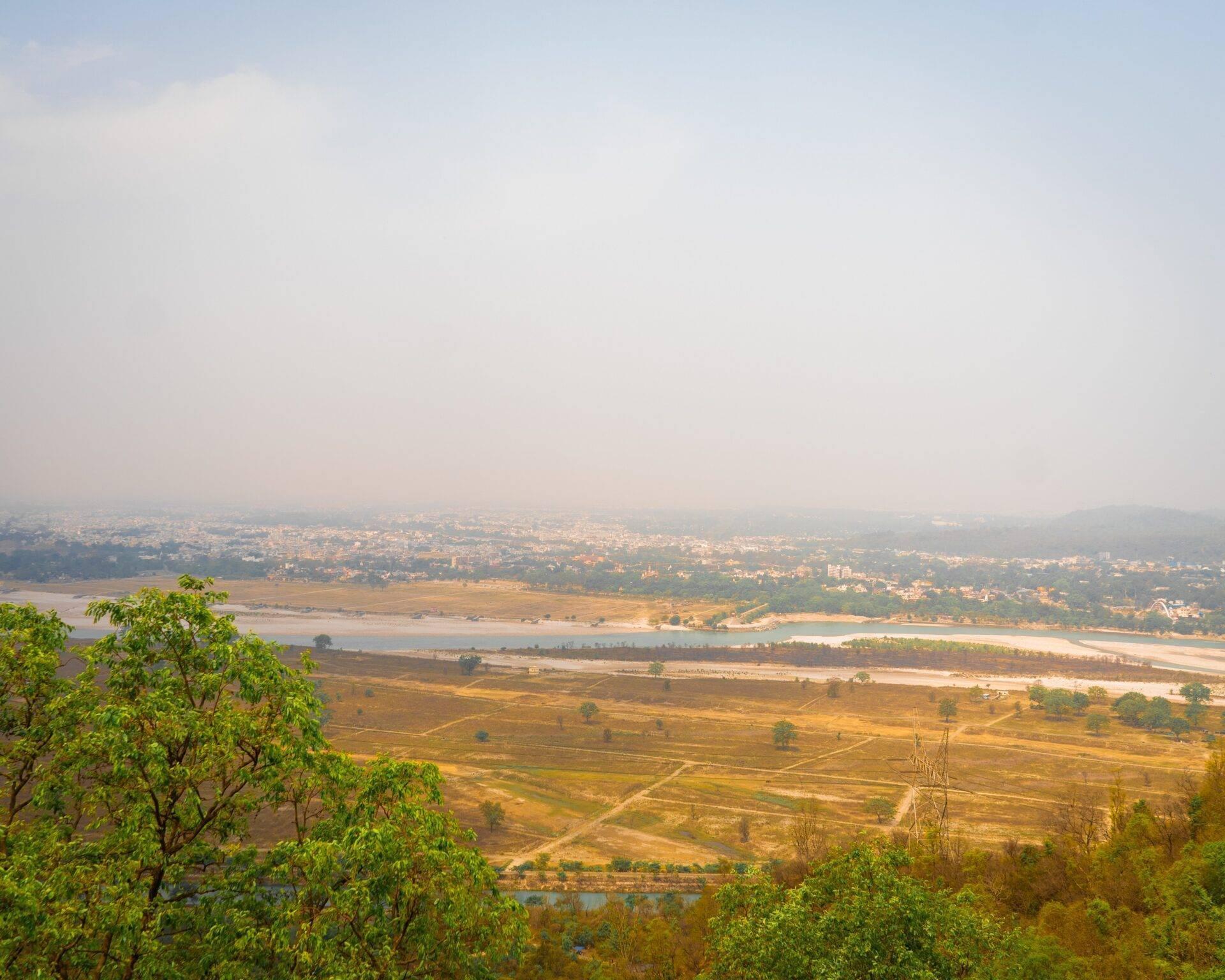 Vista panoramica di una valle fluviale con risaie, villaggi sparsi e nebbia atmosferica sullo sfondo