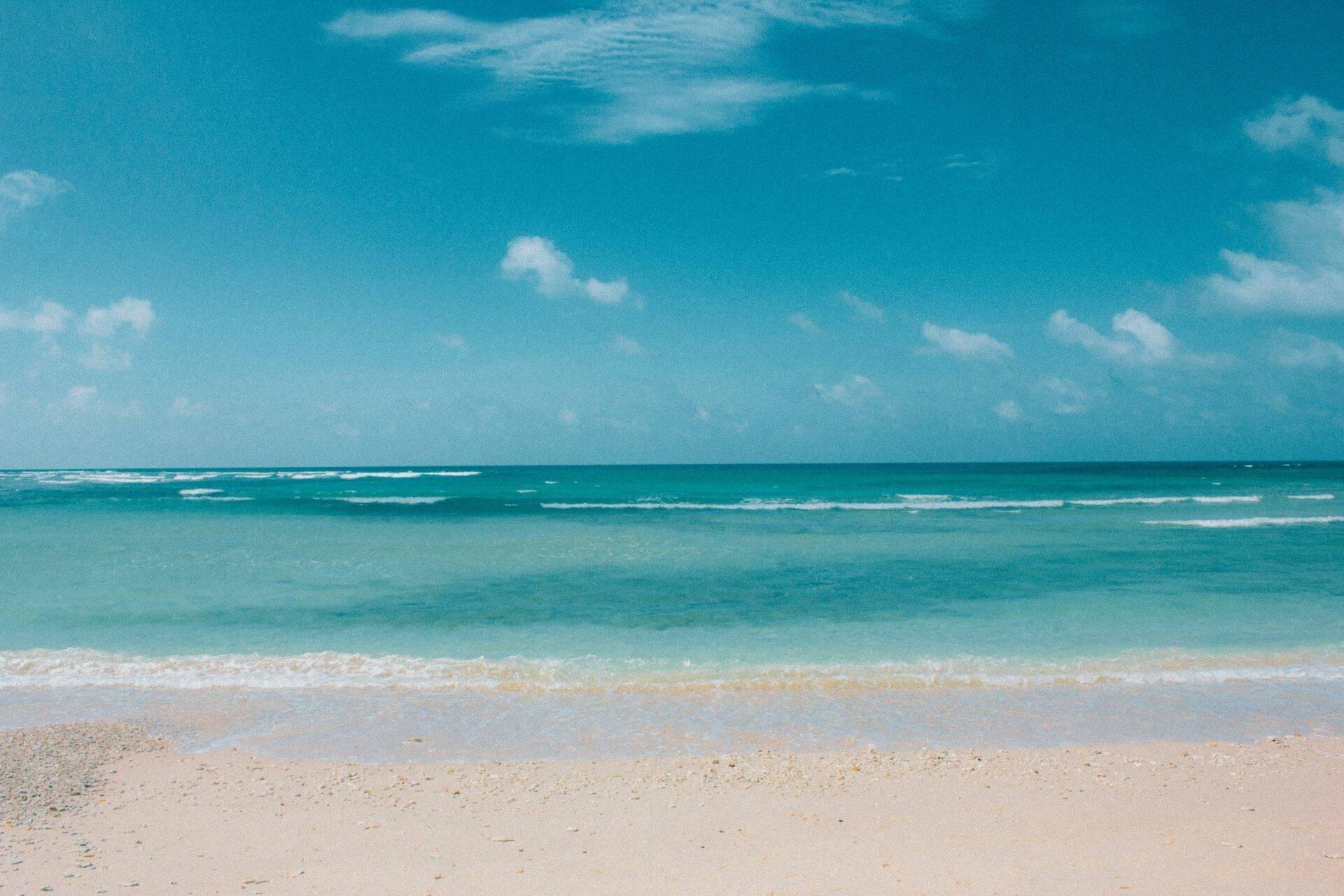 Playa de arena blanca con aguas turquesas cristalinas y cielo azul despejado, imagen de paraíso tropical
