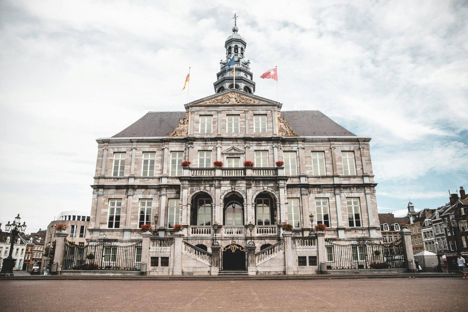 Historisches Steingebäude mit Turm, Flaggen und Balustraden auf einem gepflasterten Platz