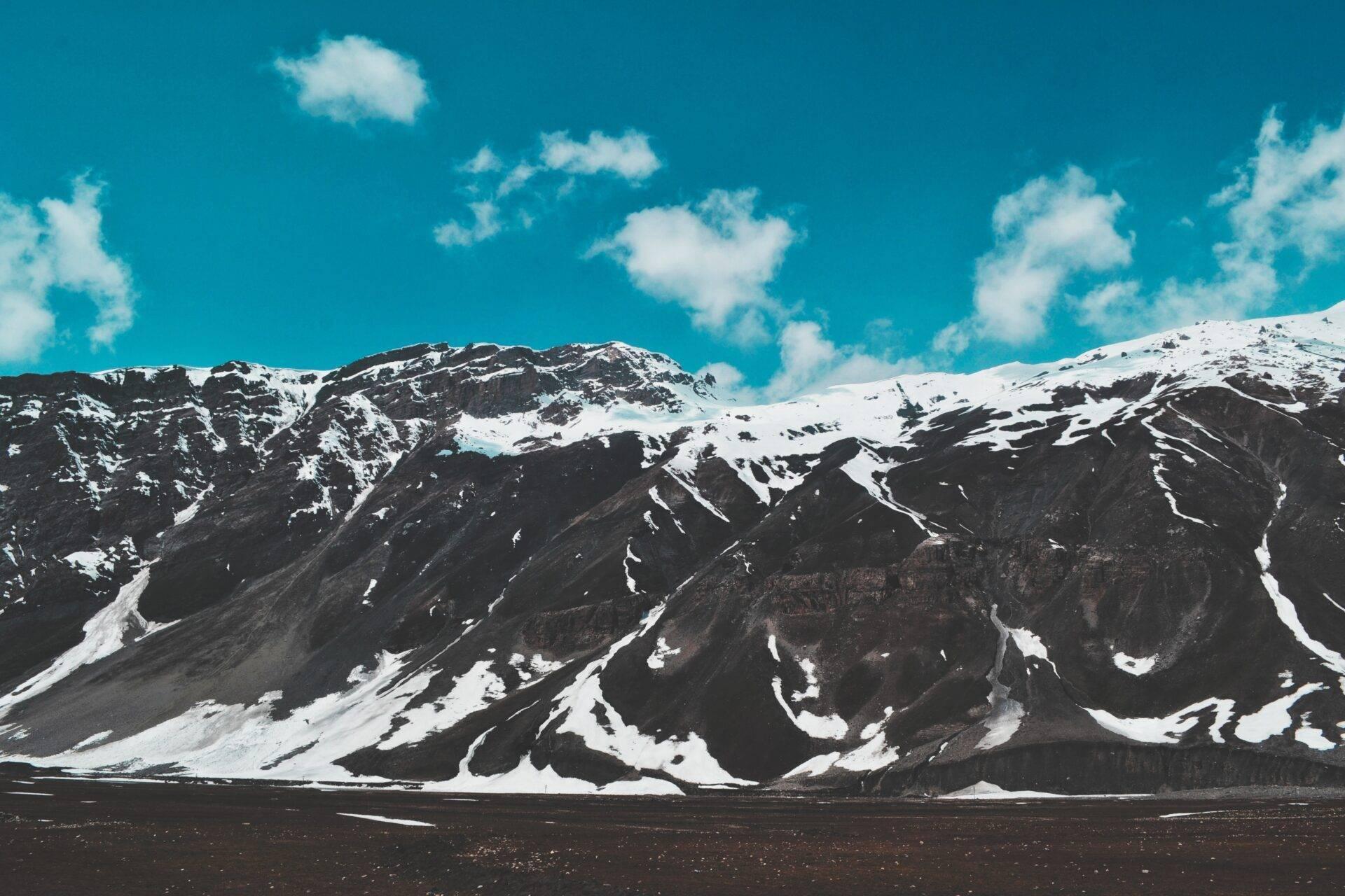 Catena montuosa innevata con pendii rocciosi scuri e cielo azzurro terso, paesaggio desertico alpino spettacolare