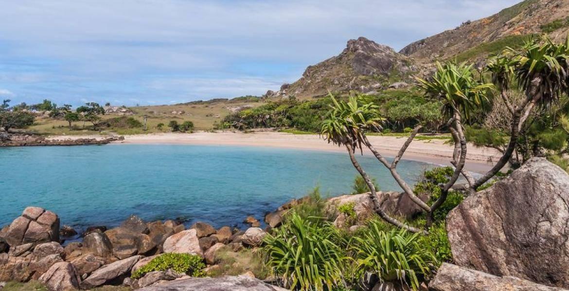 Una baia tropicale dalle acque turchesi bordata da una spiaggia di sabbia bianca, rocce granitiche e vegetazione verdeggiante