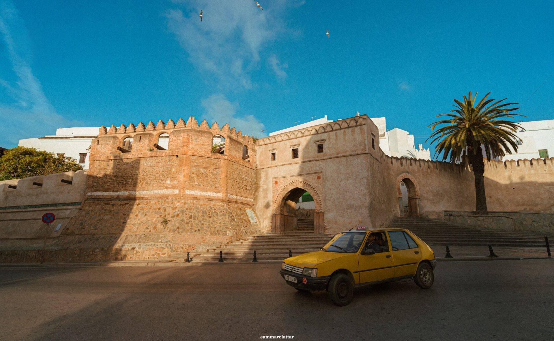 Ein gelbes Taxi vor den Steinmauern einer marokkanischen Medina unter klarem blauen Himmel