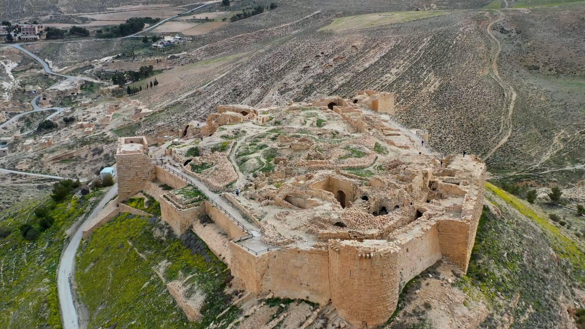 Fortaleza en ruinas vista desde arriba con muros de piedra, que domina un paisaje montañoso árido y un valle verde al fondo