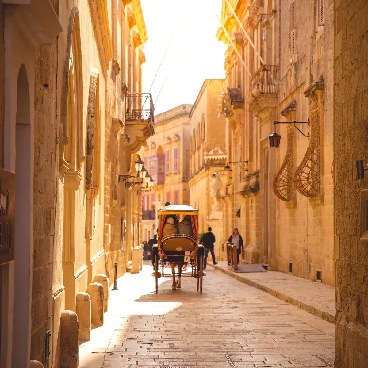 Eine gepflasterte ockerfarbene Gasse mit einer Touristenkutsche, in warmem Licht gebadet und von historischen Fassaden gesäumt