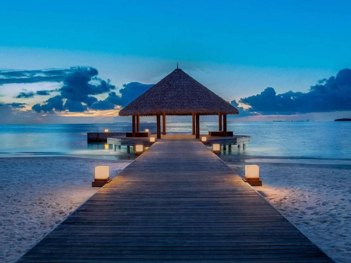 Un pontile di legno illuminato che conduce a un gazebo con tetto di paglia su una spiaggia tropicale al tramonto