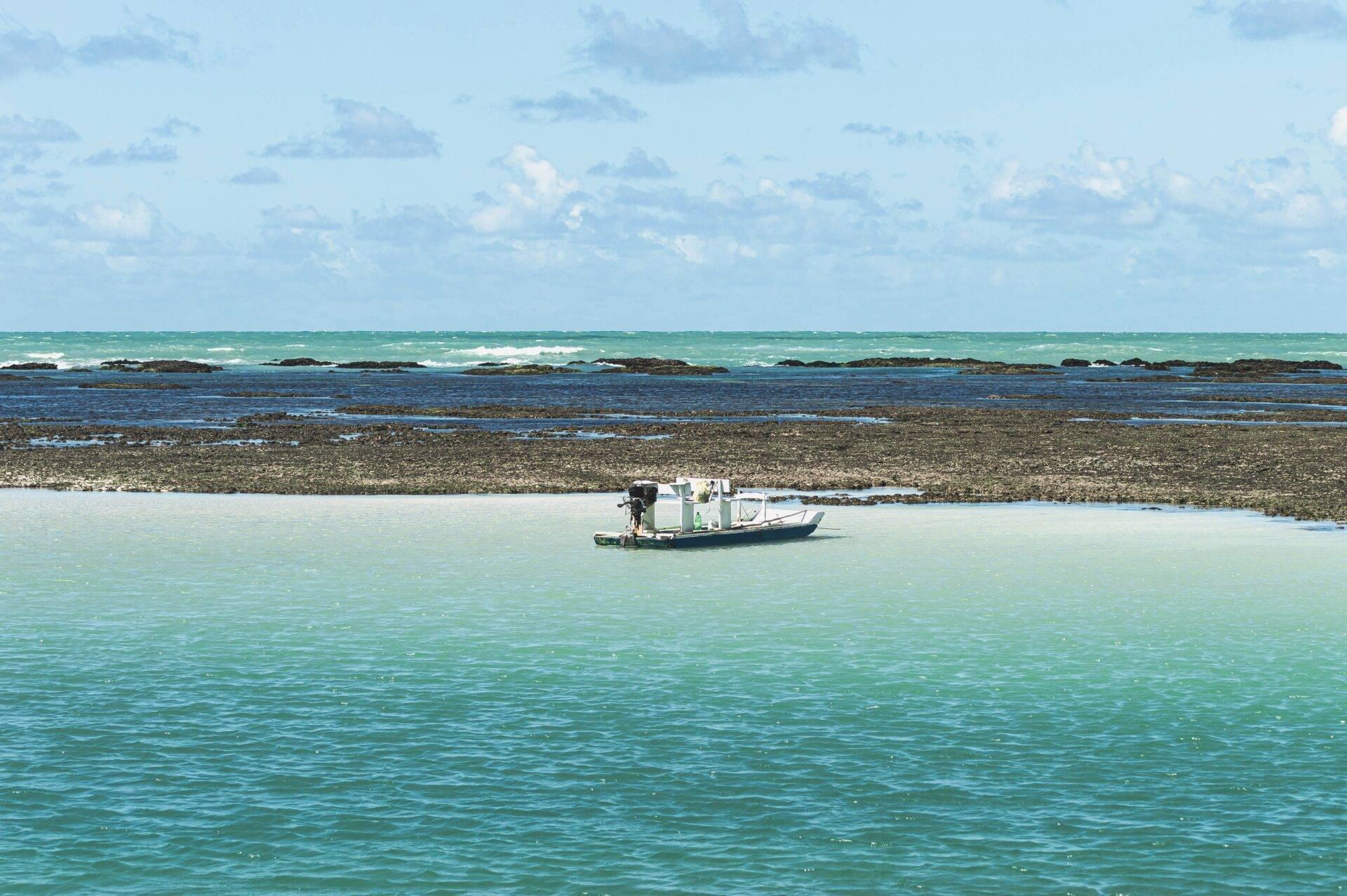 A small white fishing boat moored in shallow turquoise waters near a rocky beach