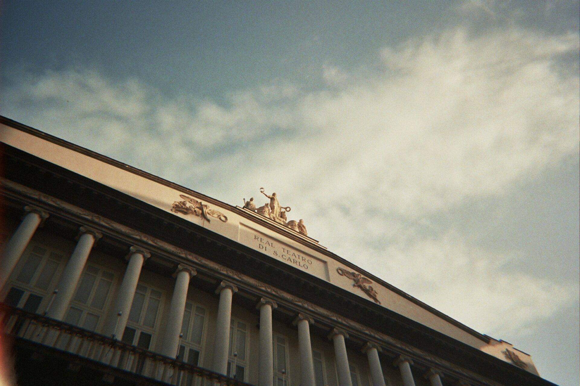Facade of a historic Italian theatre with classical columns and gilded statues on the roof
