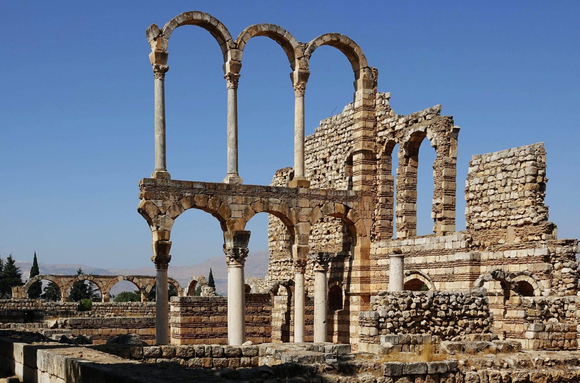 Ruinas romanas antiguas con columnas y arcos de piedra bajo un cielo despejado, montaña al fondo