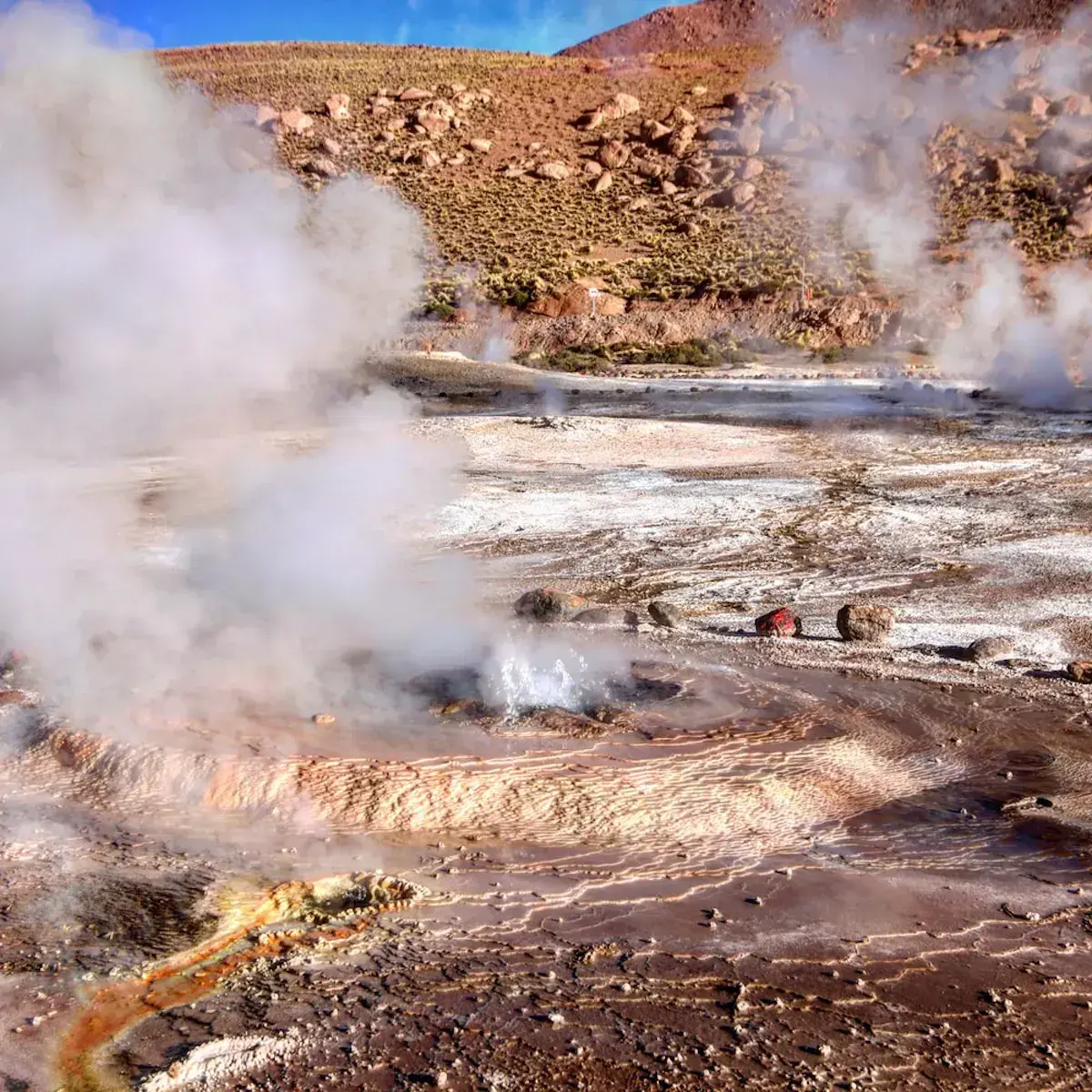 Géiser y fuentes termales humeantes en un paisaje desértico mineral de colores ocres y blancos
