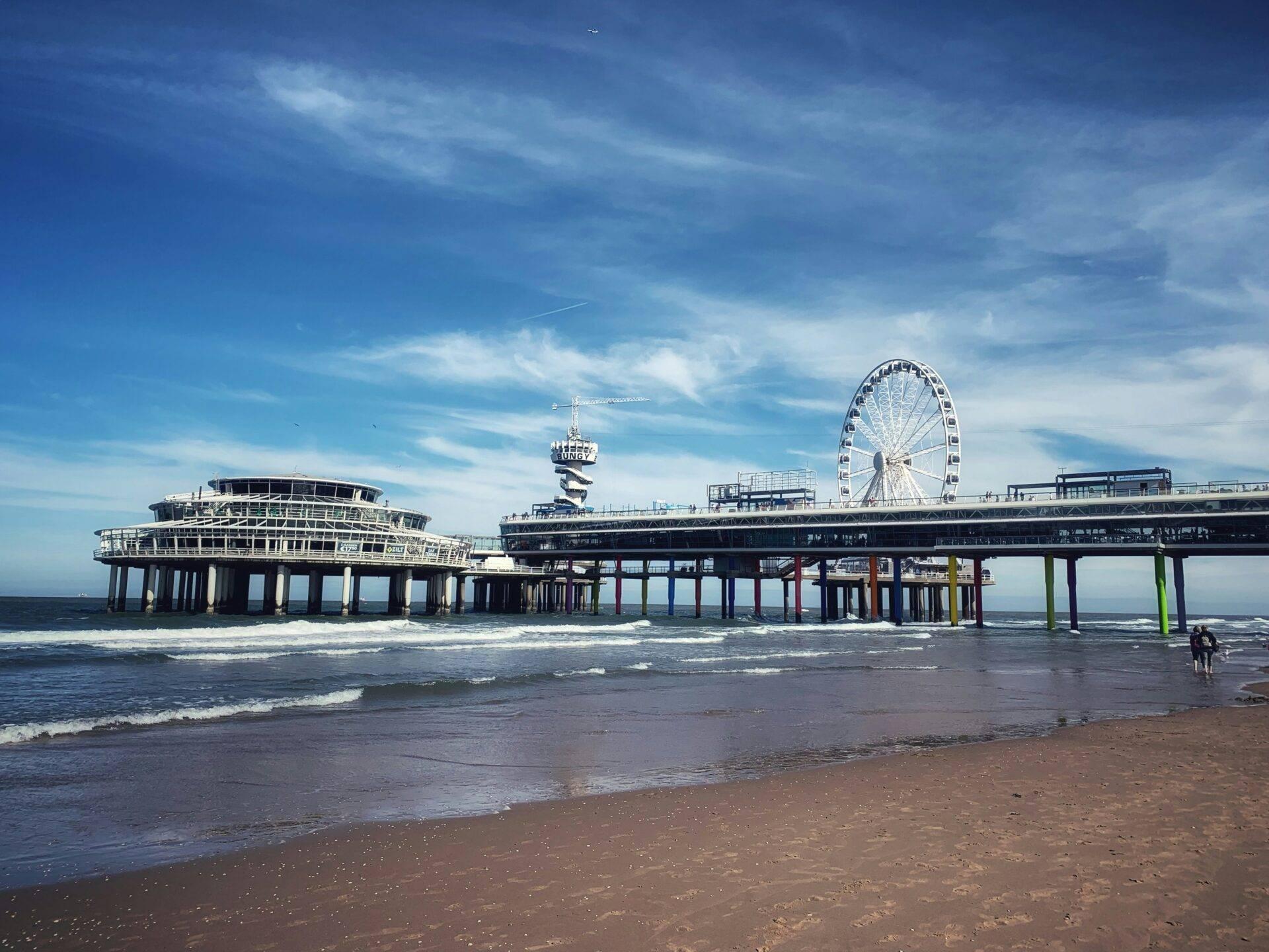Küstenpier mit Riesenrad, Attraktionen und Sandstrand unter bewölktem blauem Himmel
