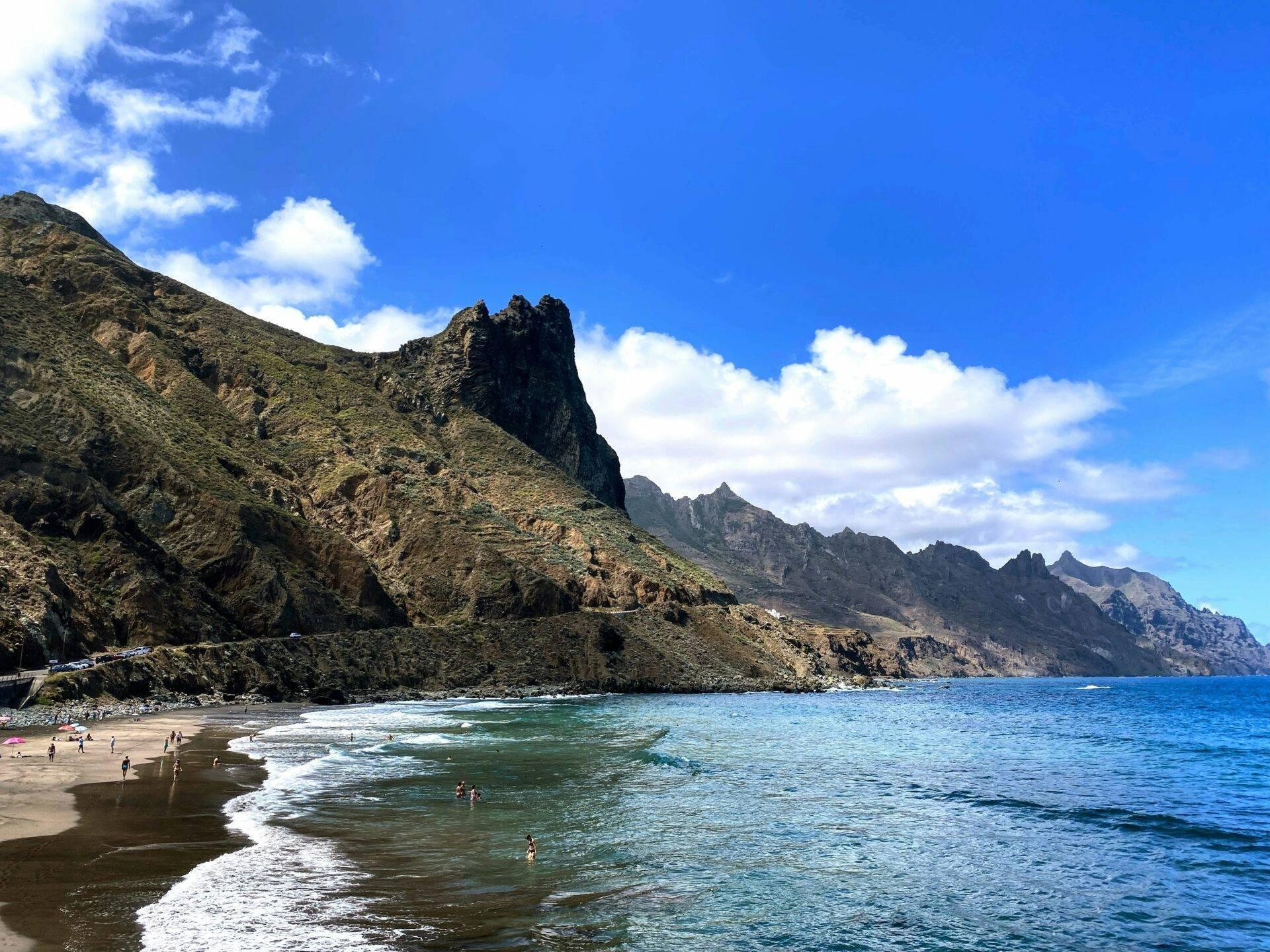 Una spiaggia di sabbia nera incorniciata da spettacolari scogliere rocciose con bagnanti e un mare turchese
