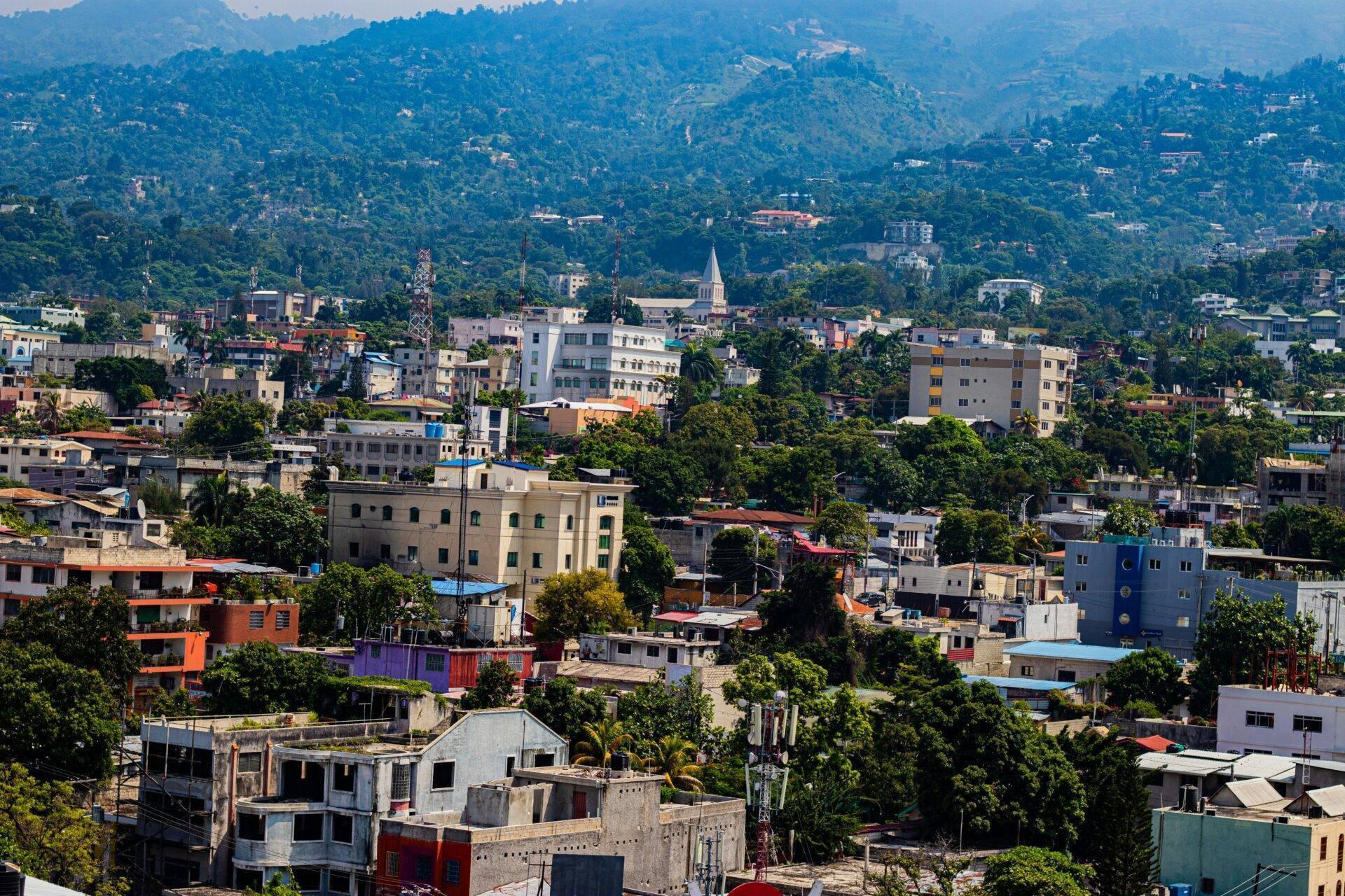 Vista aérea de una ciudad tropical de montaña con edificios de colores, densa vegetación y una iglesia blanca en el centro