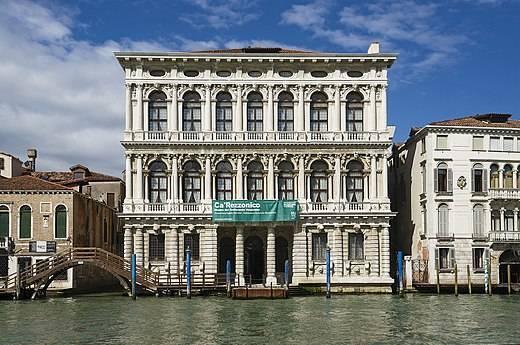 Un palazzo veneziano bianco dalle facciate ornate si affaccia sul Canal Grande sotto un cielo azzurro limpido