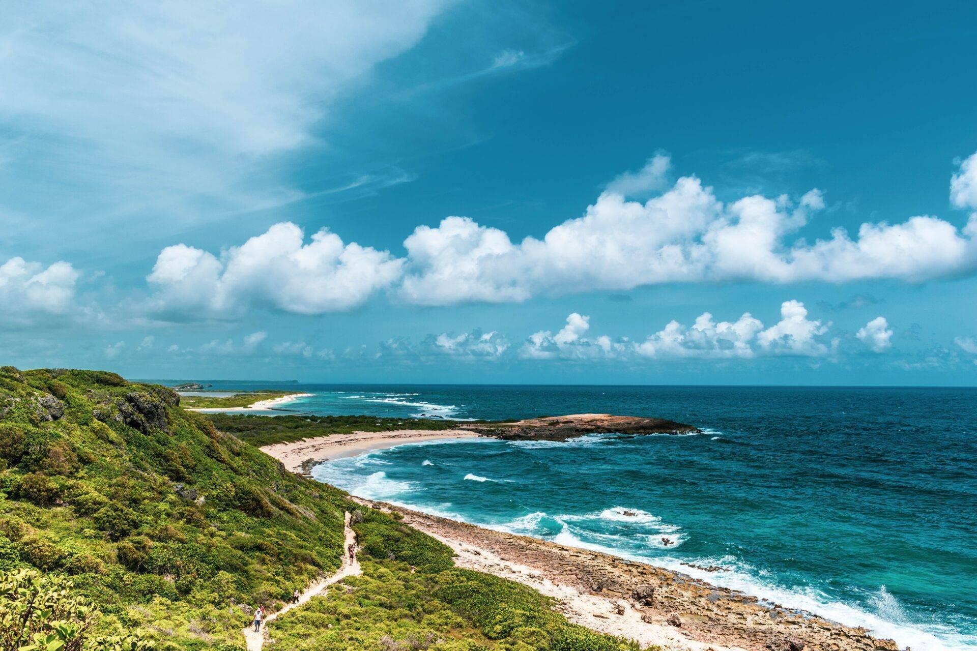 Grüne Steilküste über einer Küstenbucht mit Sandstränden und Felsen unter blauem Himmel mit weißen Wolken