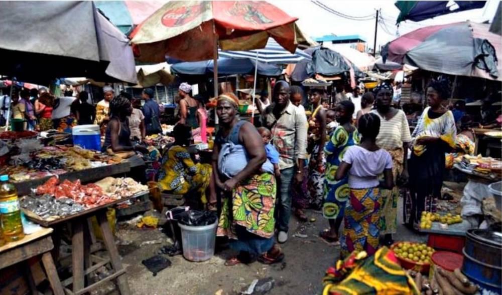 Un mercato colorato nell’Africa occidentale con venditori, bancarelle di frutta e verdura, ombrelloni e folla animata
