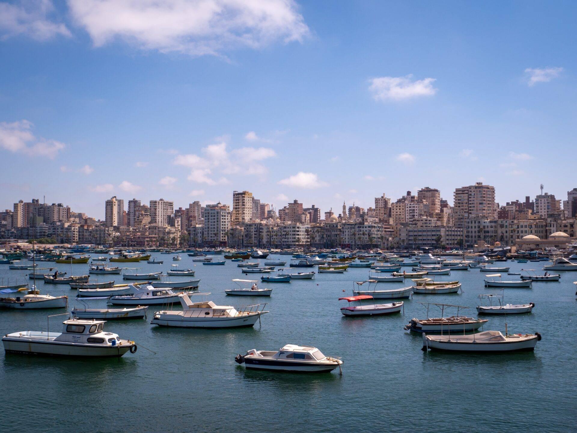 Baia costiera mediterranea con decine di piccole barche da pesca e un immenso skyline urbano densamente costruito sullo sfondo