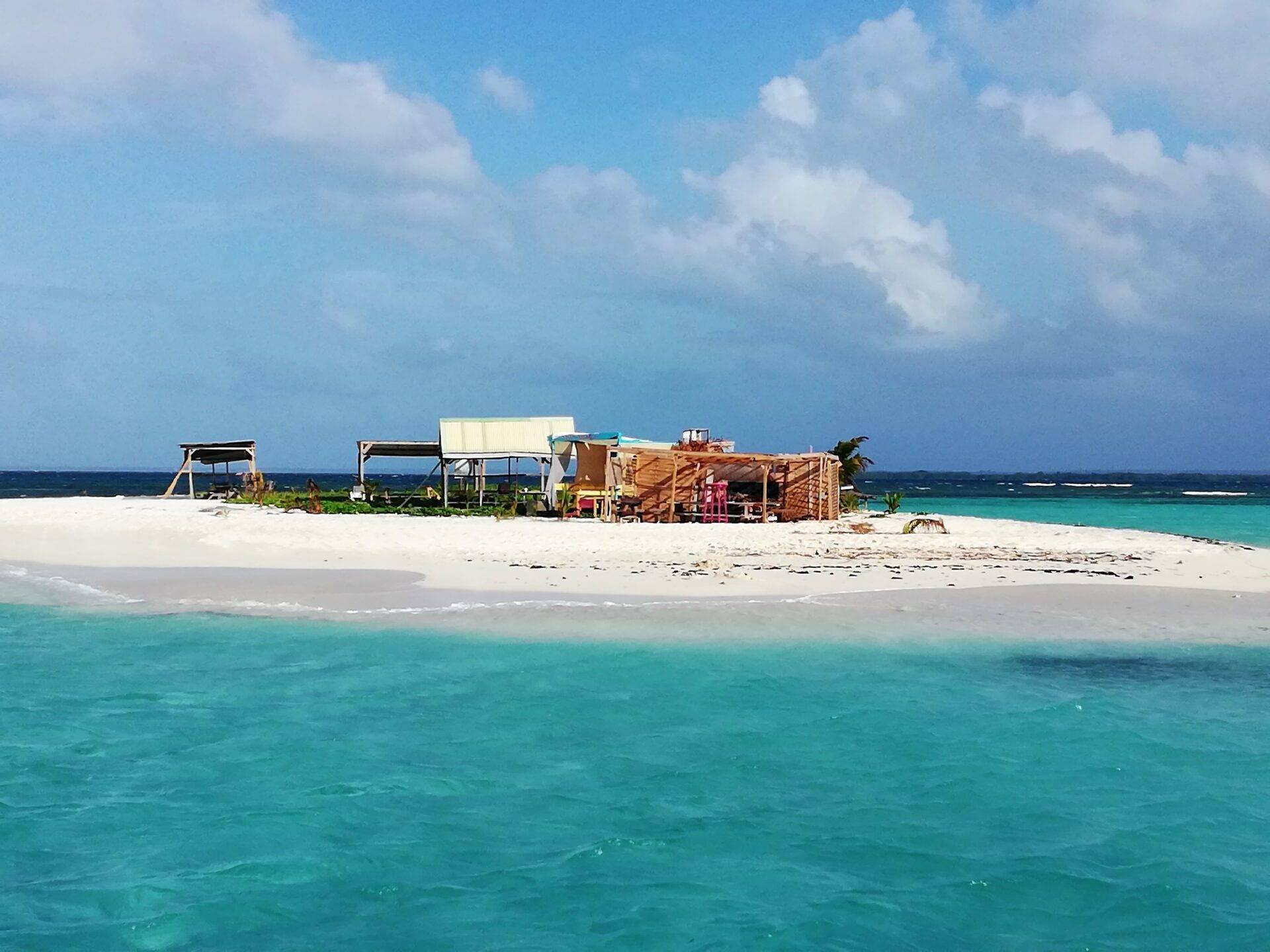 Ein einsamer Tropenstrand mit Holzhütten, kristallklarem Türkisblau und bewölktem blauem Himmel