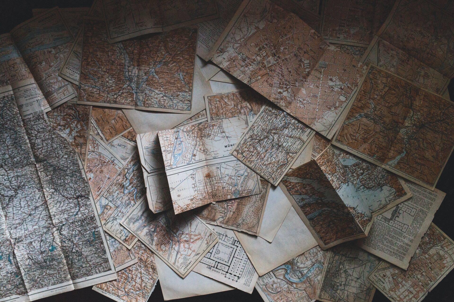 Sammlung alter geographischer Karten und Stadtpläne auf einer weißen Fläche, die an die Vorbereitung einer Reise erinnern