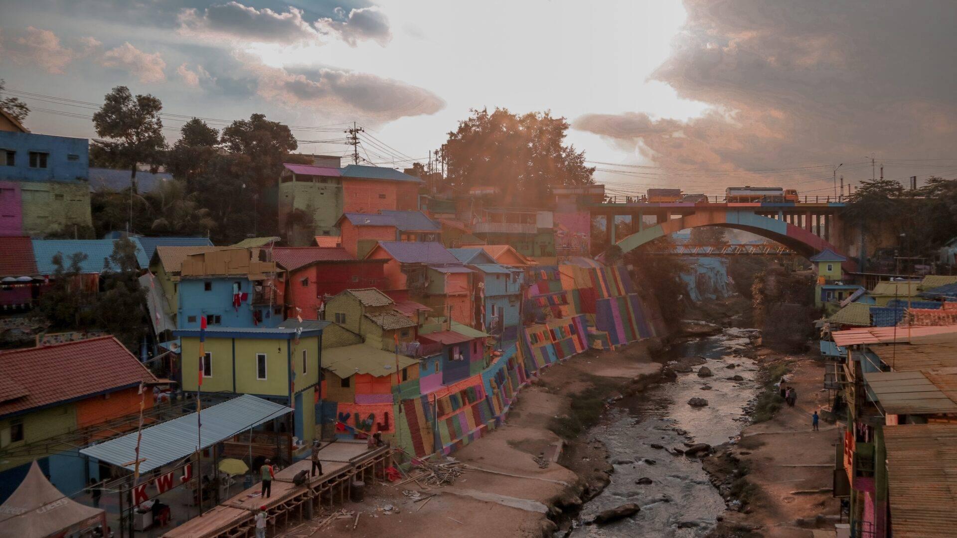 Villaggio colorato sulle rive di un fiume con case dipinte in colori vivaci, ponte e cielo nuvoloso