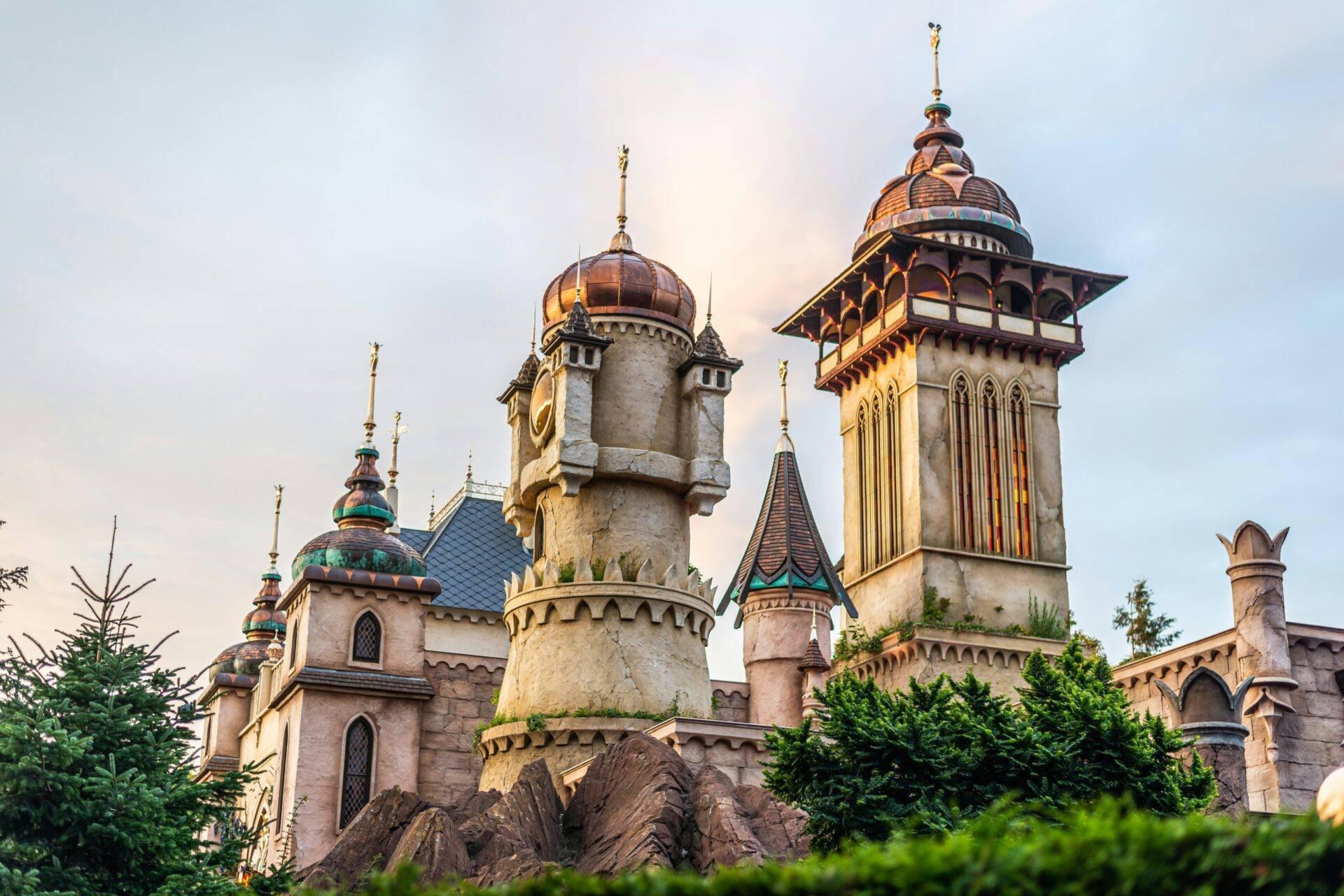 Märchenschloss mit goldenen Türmen, bunten Kuppeln und Zinnen, umgeben von Grün